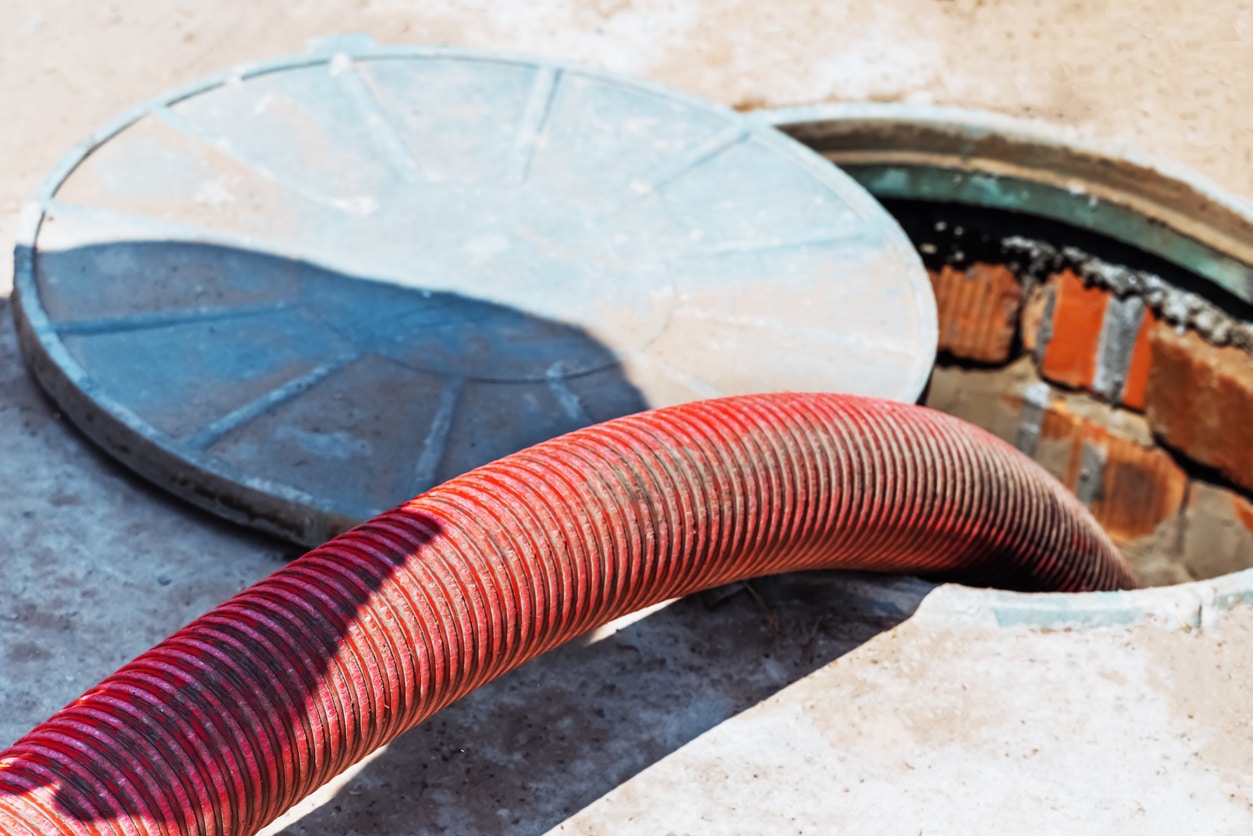 Pumping out household septic tank. drain and sewage cleaning service. Pipe in the drainage pit. Red tube inside tank, demonstrating process of expert septic pumping