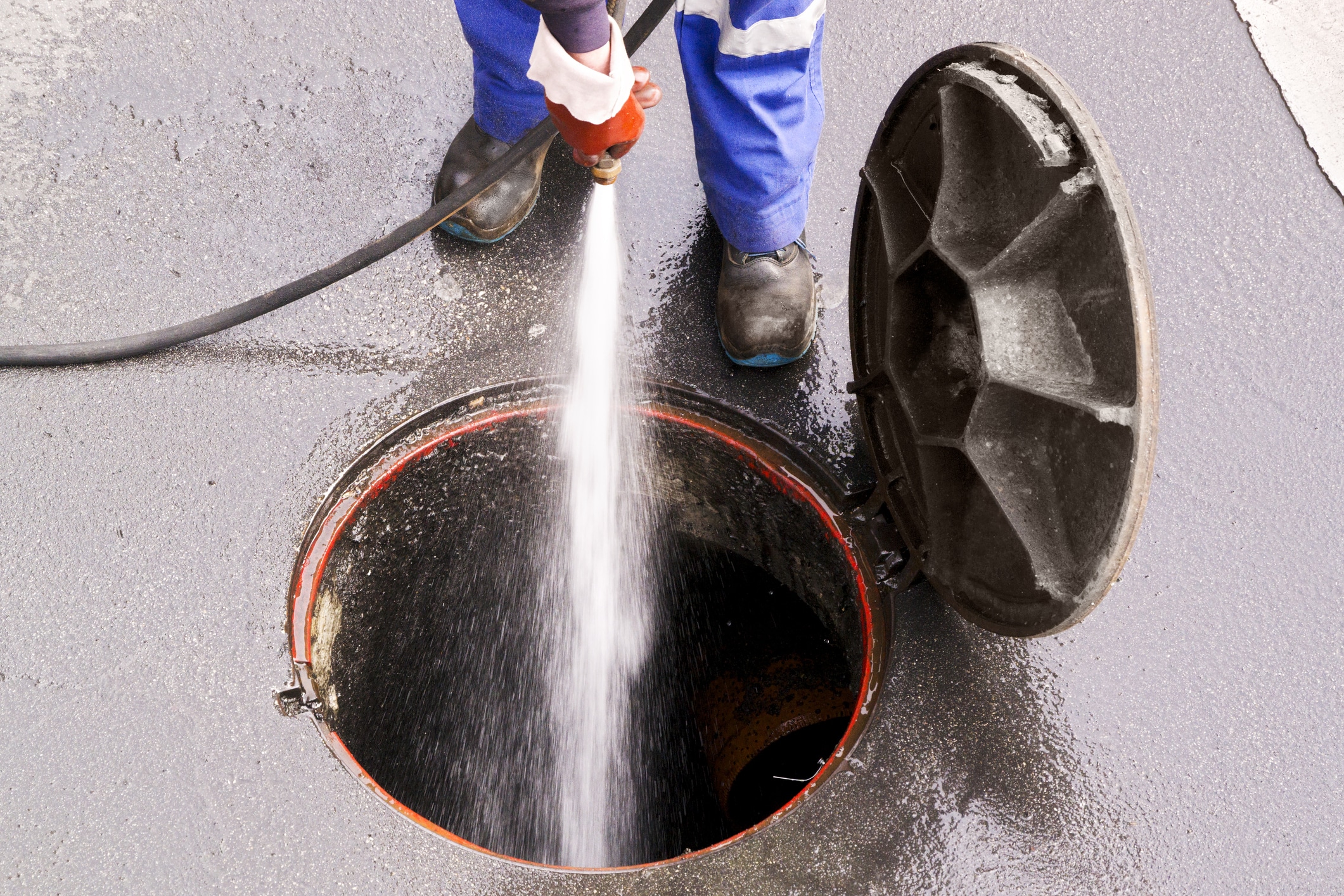 Low Section Of Man Cleaning Manhole Red tube inside tank, demonstrating process of expert septic pumping